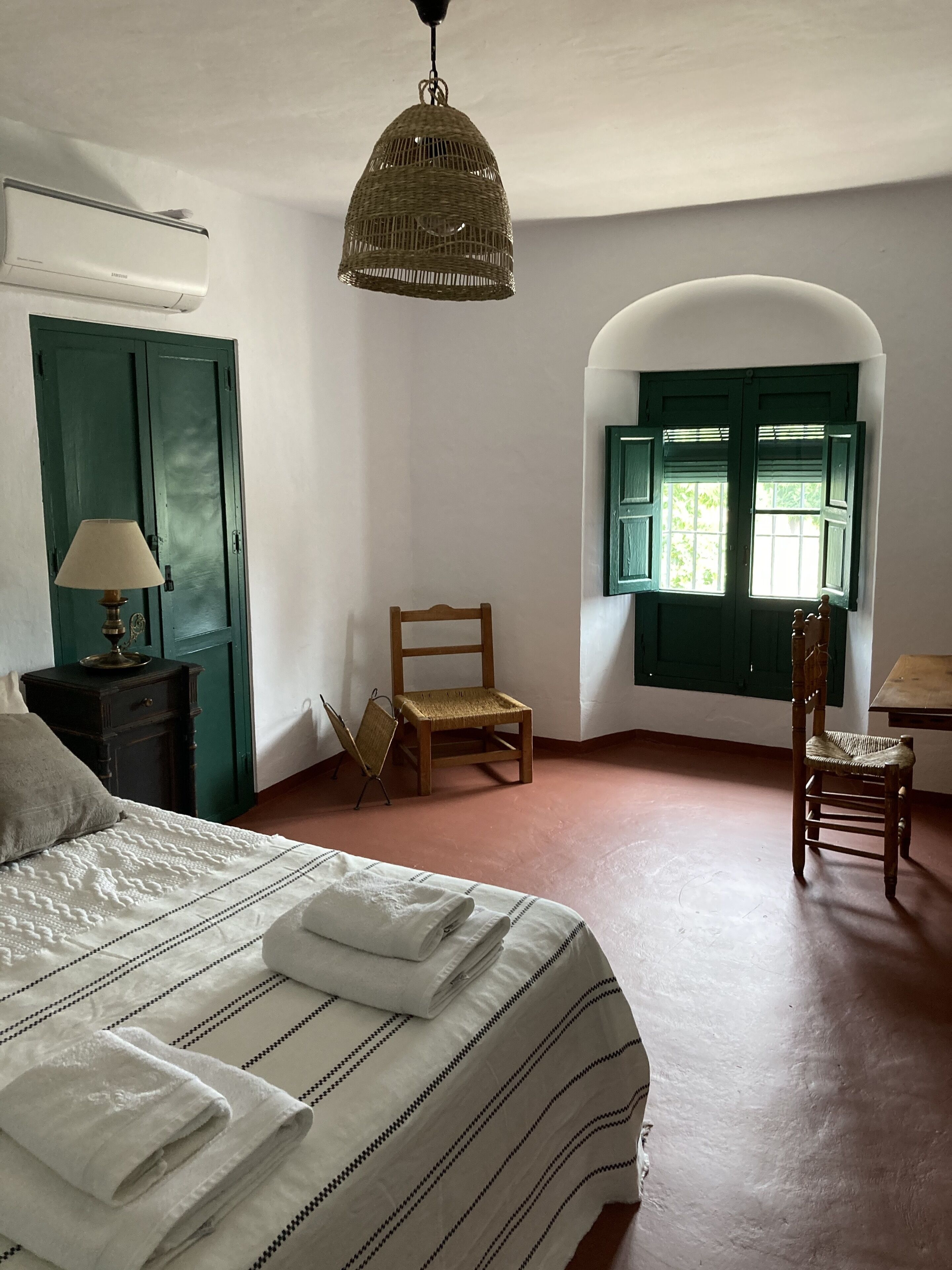 Un dormitorio con una cama, una silla, una mesa y una ventana con contraventanas verdes.