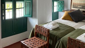 Een kamer met een bed, een stoel, een hanglamp en ramen met groene omlijsting.