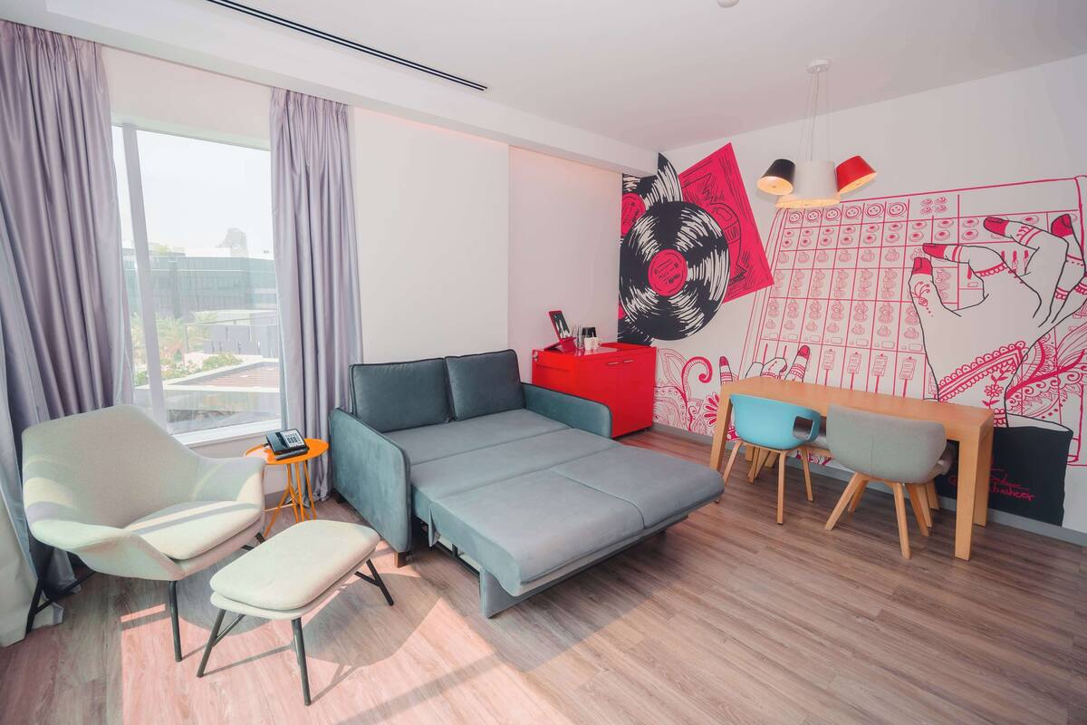 A modern room with a sofa bed, a small table, a chair, and a desk with chairs.