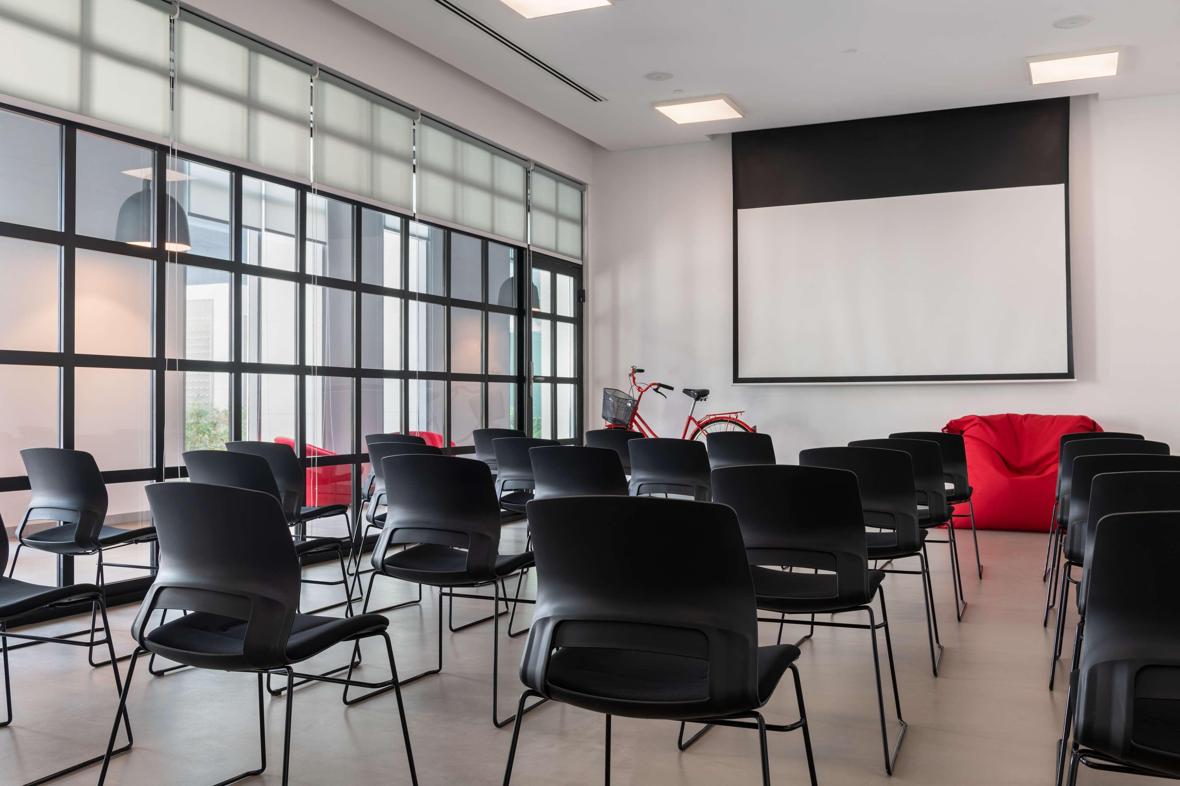Une salle de conférence avec des rangées de chaises noires, un grand tableau blanc et un fauteuil rouge en forme de sac de haricots.