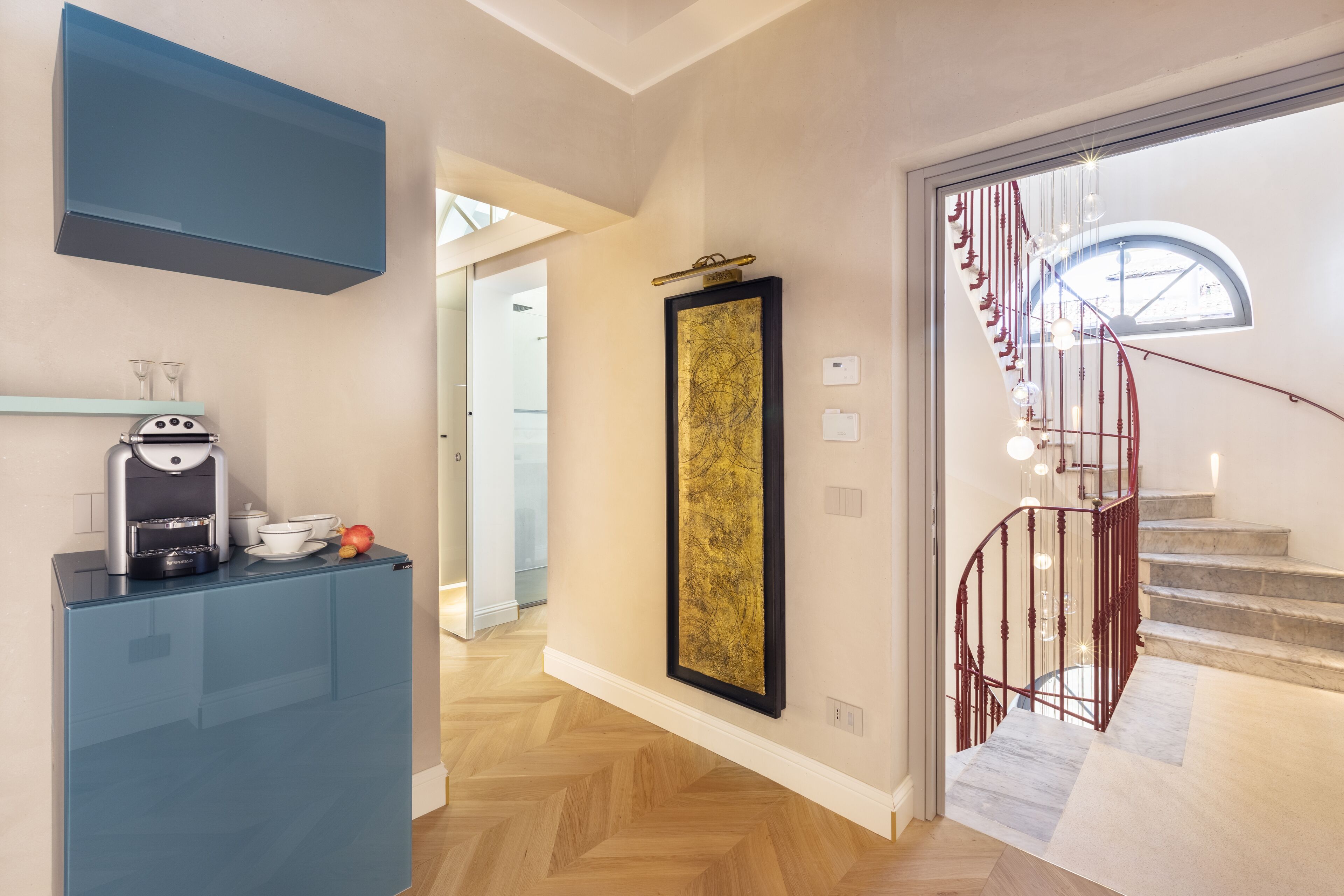 A modern kitchen with a built-in coffee machine, a large framed artwork, and a staircase leading to an upper floor.