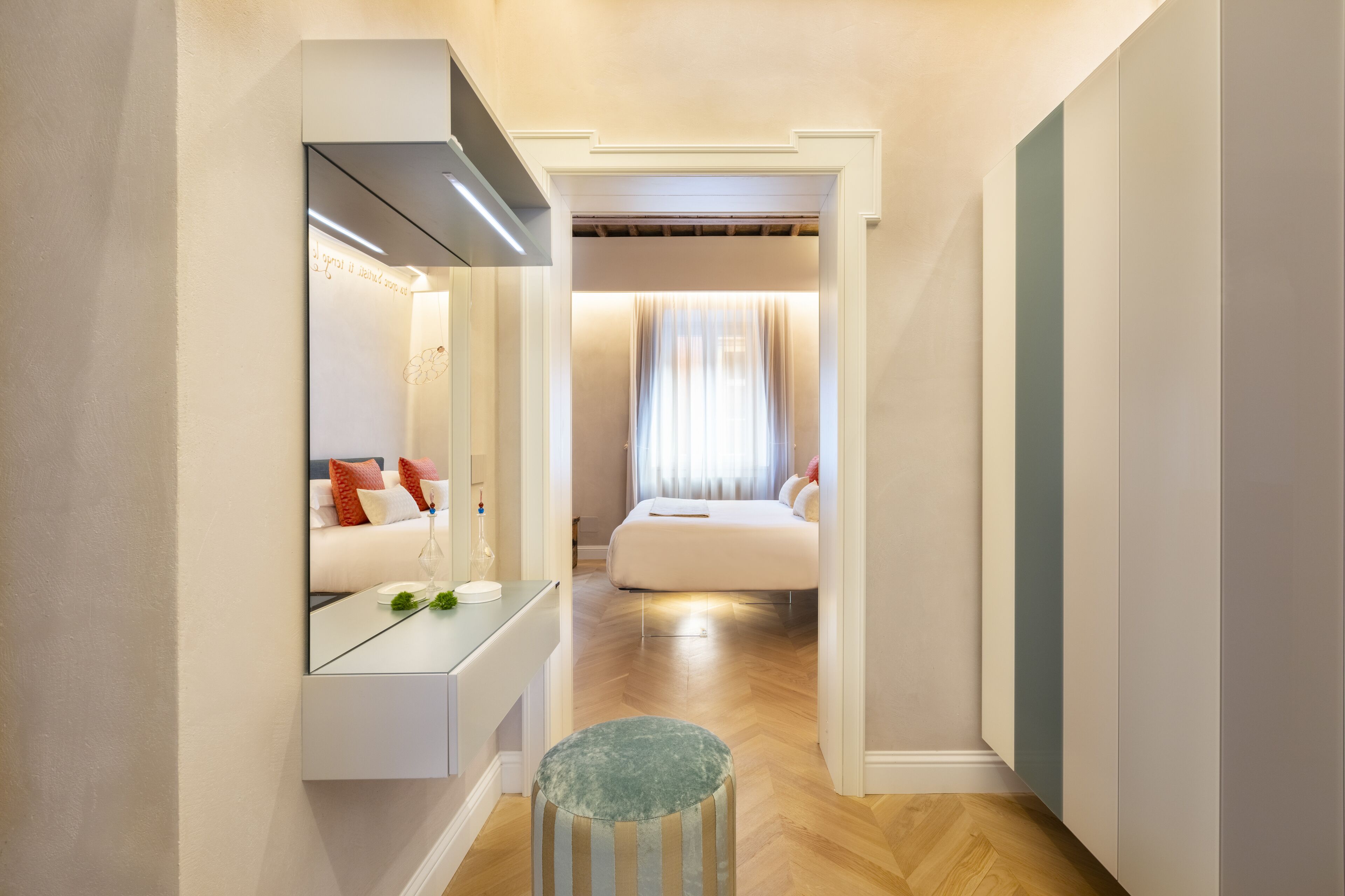 Un pasillo que da a un dormitorio con cama, un espejo y un pequeño taburete.