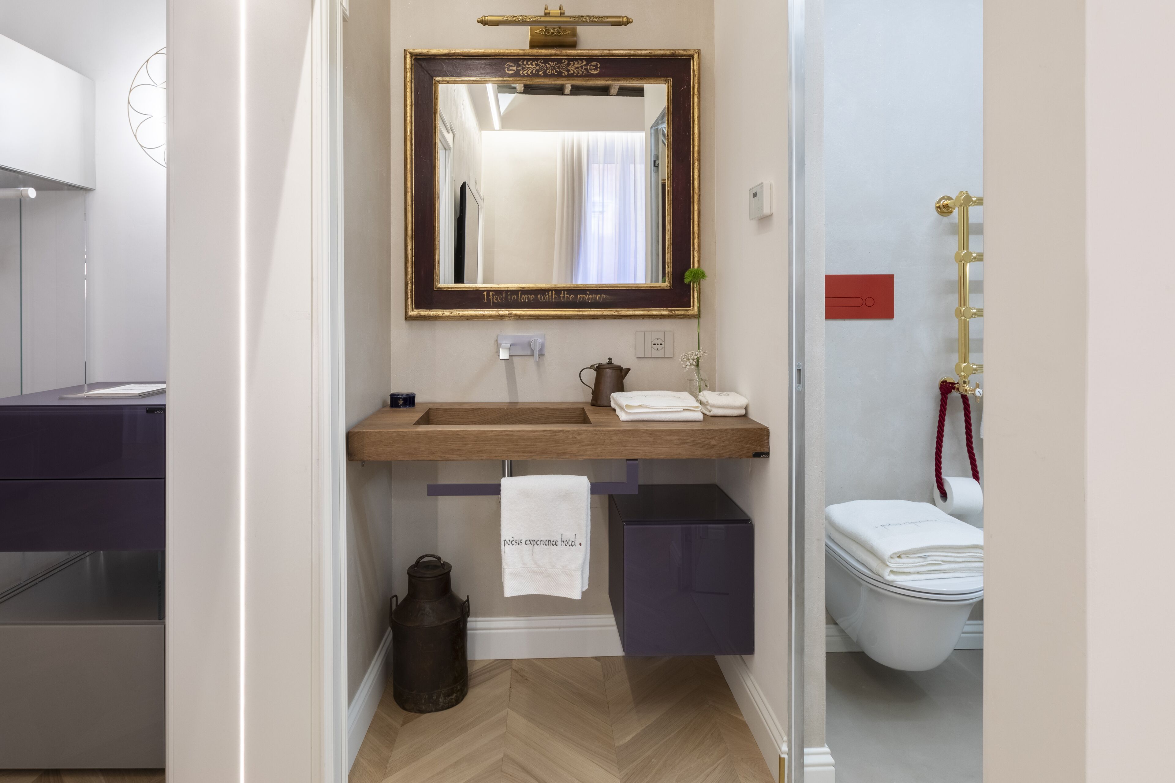 A bathroom with a wooden vanity, a mirror with a decorative frame, a towel hanging on a rack, and a toilet.