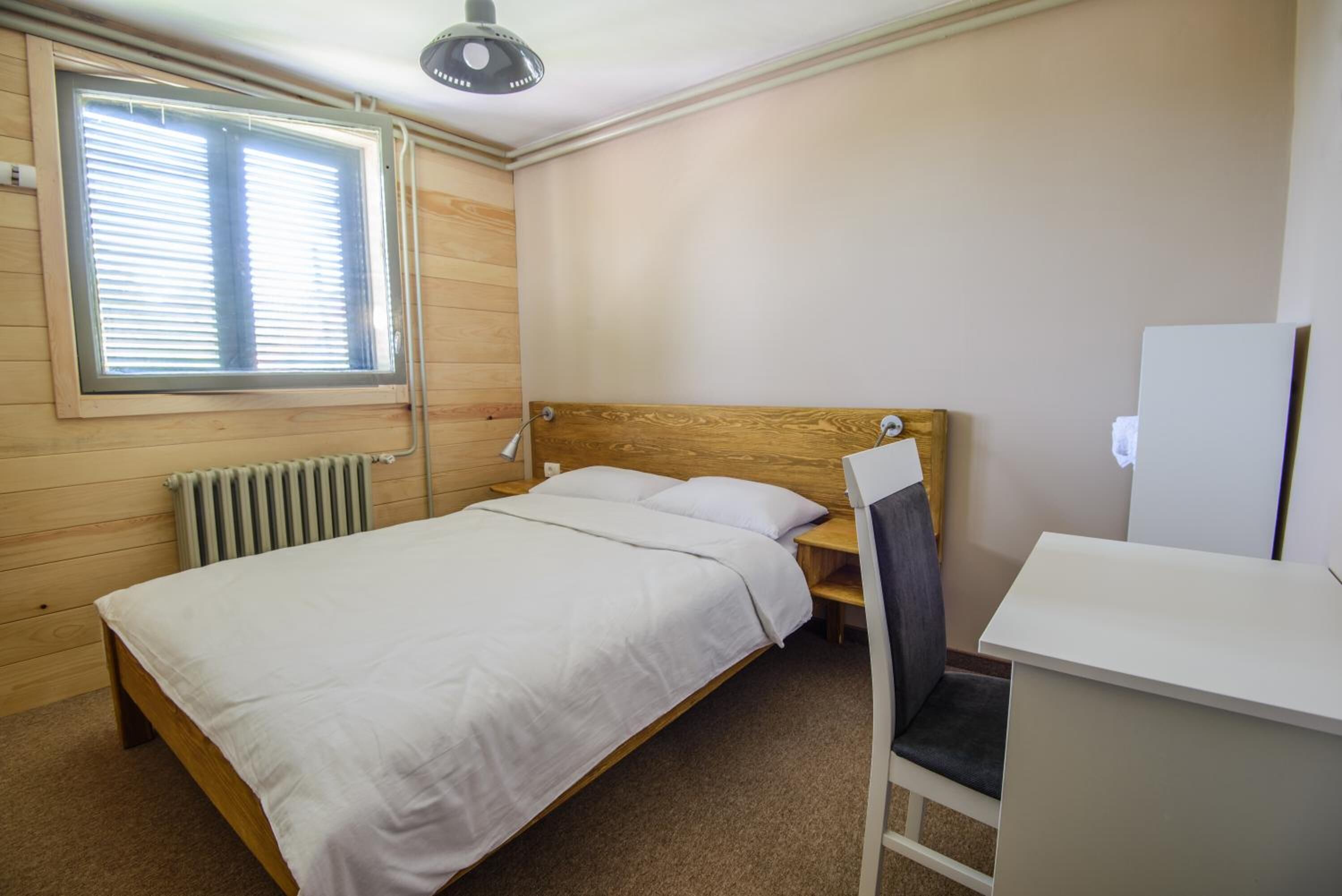 Una cama individual con cabecera de madera, una mesita de noche, una silla y un radiador.