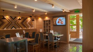 Un restaurante con paredes, mesas y sillas de madera. Se ve una pantalla de televisión mostrando comida, y un letrero de salida es visible.