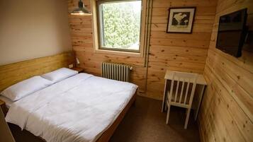 A wooden cabin bedroom with a bed, a window, a radiator, and a chair.