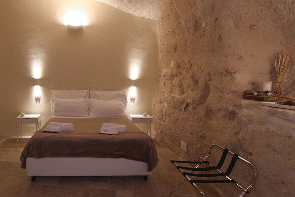 A bedroom with a bed, two bedside tables, a chair, and a stone wall. - Il Casale di Maria (Matera)