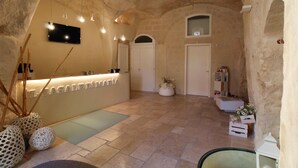 A spacious interior with a reception desk, a flat-screen TV, and a stone wall. - Il Casale di Maria (Matera)