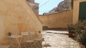 A cobblestone courtyard with white folding chairs and a small table, surrounded by stone walls and potted plants. - Il Casale di Maria (Matera)
