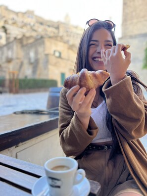 A person sitting at an outdoor table with a cup of coffee and a pastry. - Il Casale di Maria (Matera)