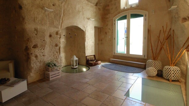 A spacious room with a high ceiling, stone walls, a large arched doorway, and a window with a view. - Il Casale di Maria (Matera)