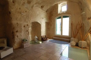 A spacious room with a high ceiling, stone walls, a large arched doorway, and a window with a view. - Il Casale di Maria (Matera)