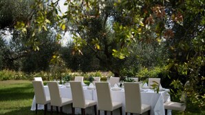 An outdoor dining area with tables set for six, surrounded by greenery and trees. - Relais d'Itria (Grottaglie)