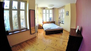 A bedroom with a large window, a bed, a bedside table, and a mirror. - Victus Apartamenty - Etna (Sopot)