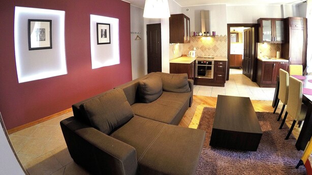 A modern living room with a brown sofa, a dining area with a table and chairs, and a kitchen with wooden cabinets and a stove. - Victus Apartamenty - Etna (Sopot)