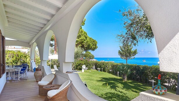 A covered outdoor area with wicker furniture, a view of the sea, and a well-maintained lawn. - Villa with direct sea access near Palermo (Carini)