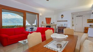 A modern living room with a red sofa, beige armchairs, and a wooden dining table with a white centerpiece. - Villa with direct sea access near Palermo (Carini)