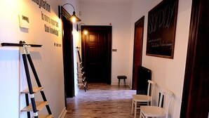 A hallway with a wooden floor, white walls, and a blackboard with writing. There are two white chairs and a black stool. - Victus Apartamenty - Flamingo (Sopot)