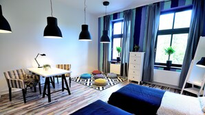 A room with a striped floor, a table with chairs, two beds, a dresser, and a window with curtains. - Victus Apartamenty - Flamingo (Sopot)