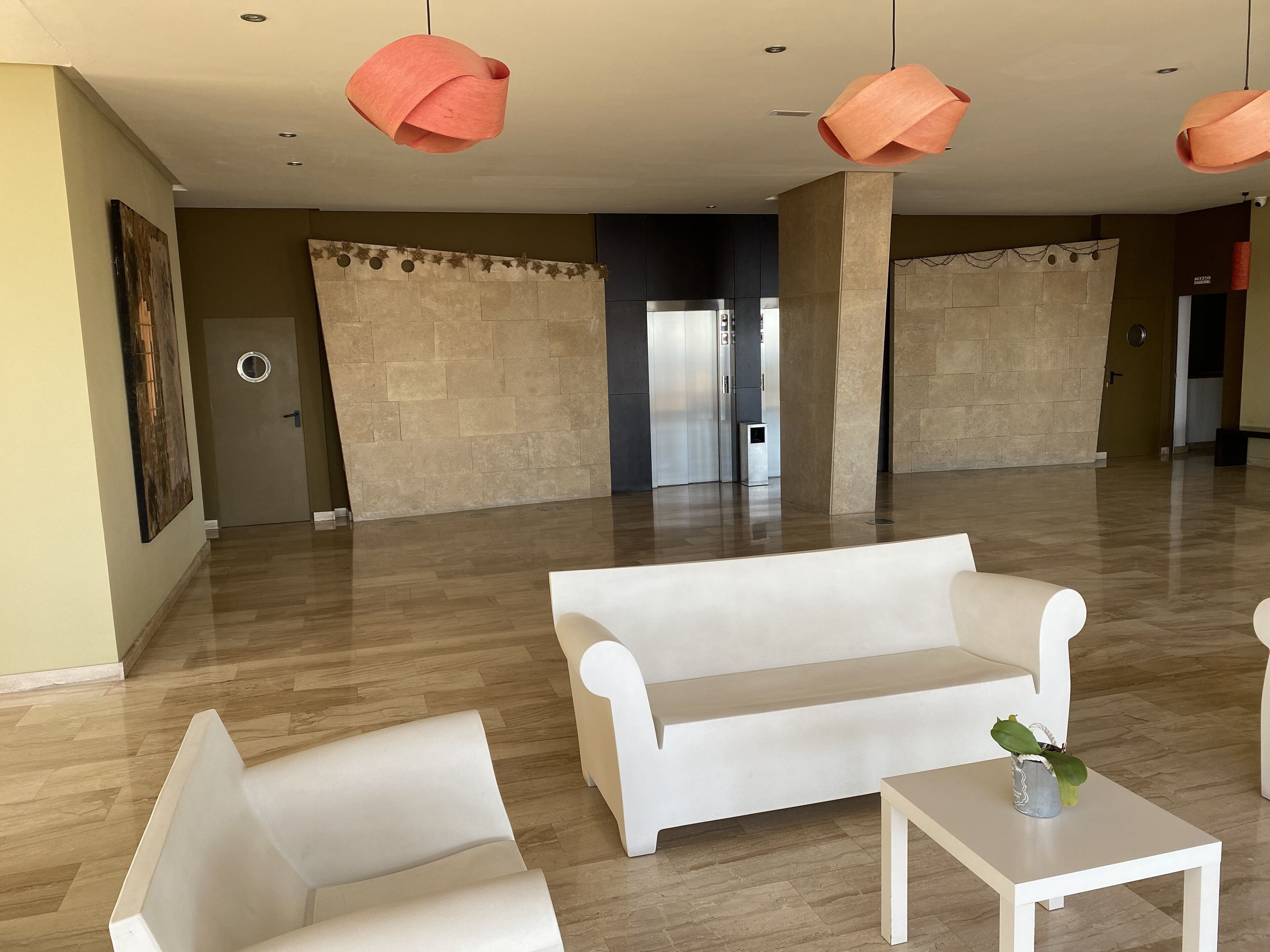 A spacious room with a white sofa, a small table, and a potted plant. There are three pendant lights hanging from the ceiling.