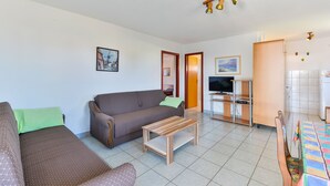 Una sala de estar con sofá, mesa de centro y una zona de televisión con aparador de madera.