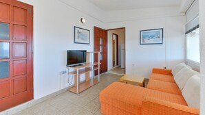 Un espacio habitable pequeño con televisión, sofá naranja y una mesita.