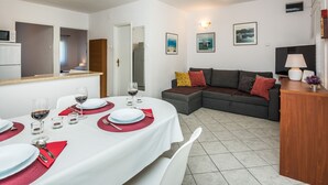 A dining area with a round table set for four, a sofa, and a wooden cabinet. - Apartment Poslon (Vir)