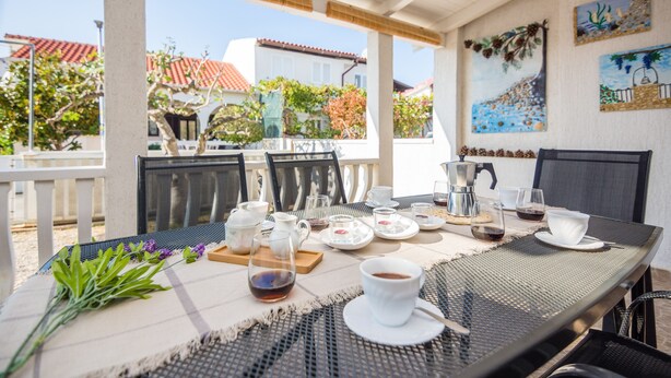 An outdoor dining area with a table set for two, featuring a coffee cup, teapot, and plates. - Apartment Poslon (Vir)