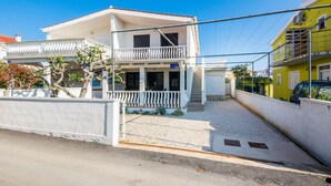 A two-story house with a balcony, a gravel driveway, and a white fence. - Apartment Poslon (Vir)