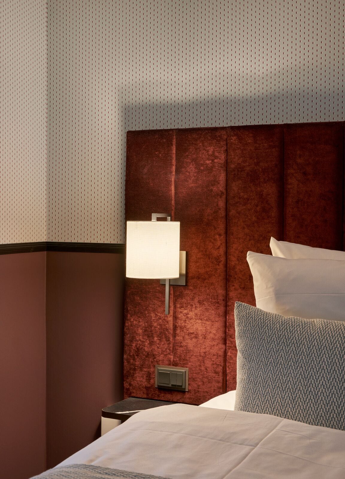 Habitación de hotel con una cama grande, una mesita de noche, una lámpara de pared y un cabecero con textura.