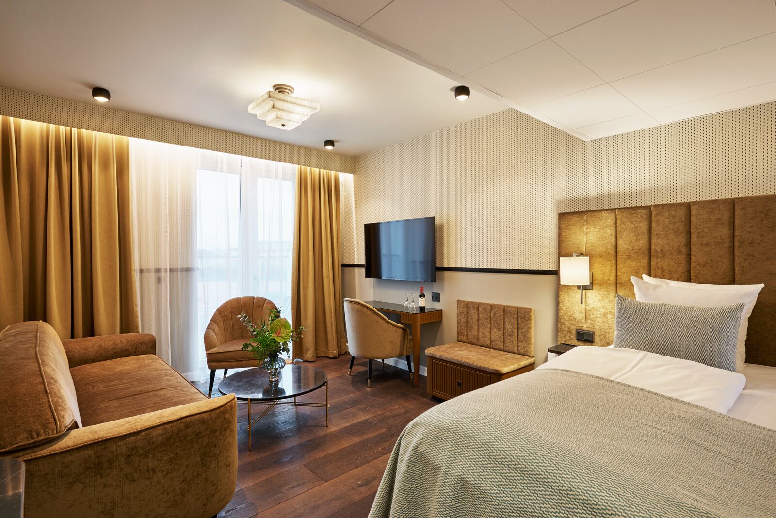 A hotel room with a large bed, a desk with a chair, a television, and a window with curtains.