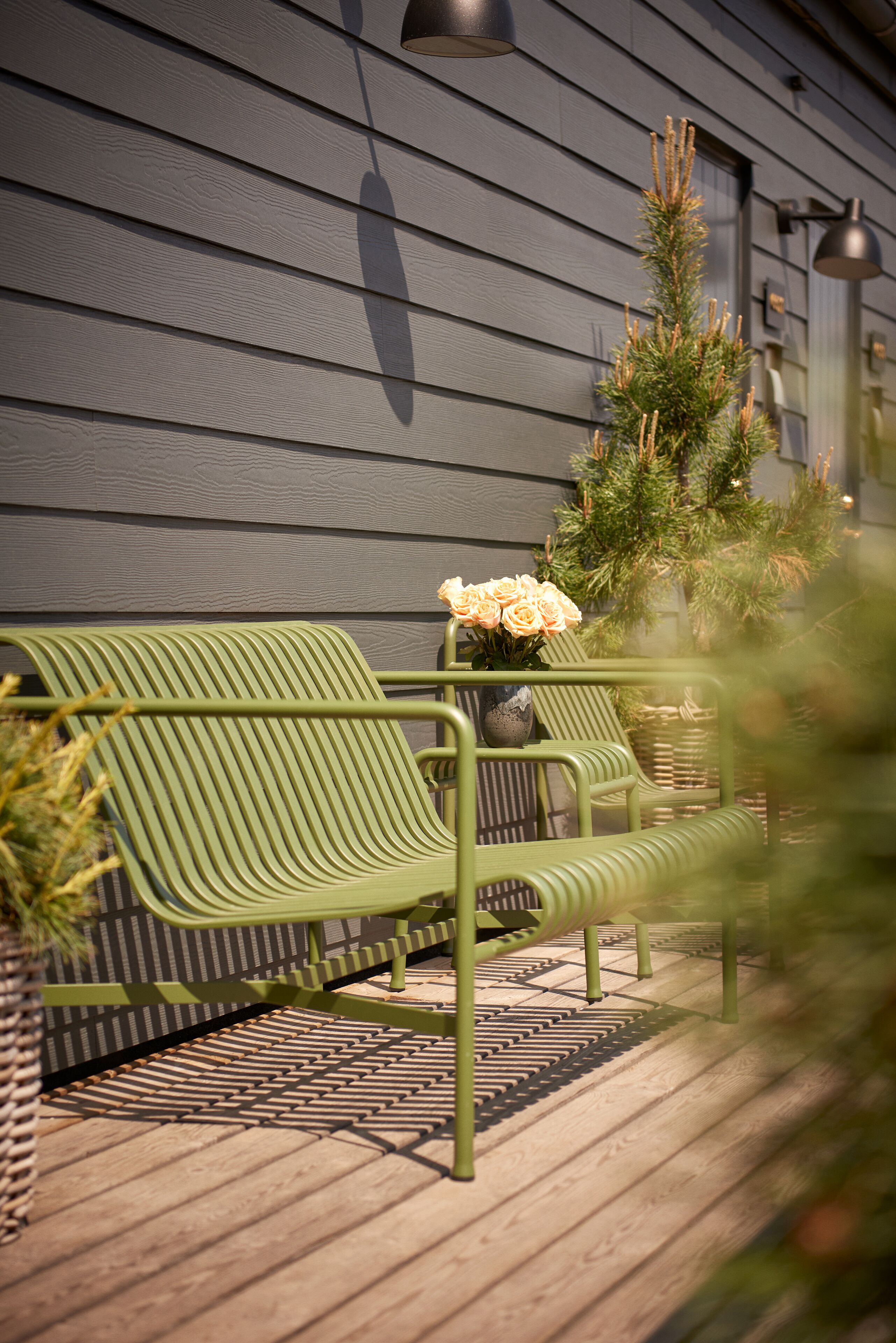 Un banc vert avec un vase de fleurs sur une terrasse en bois.