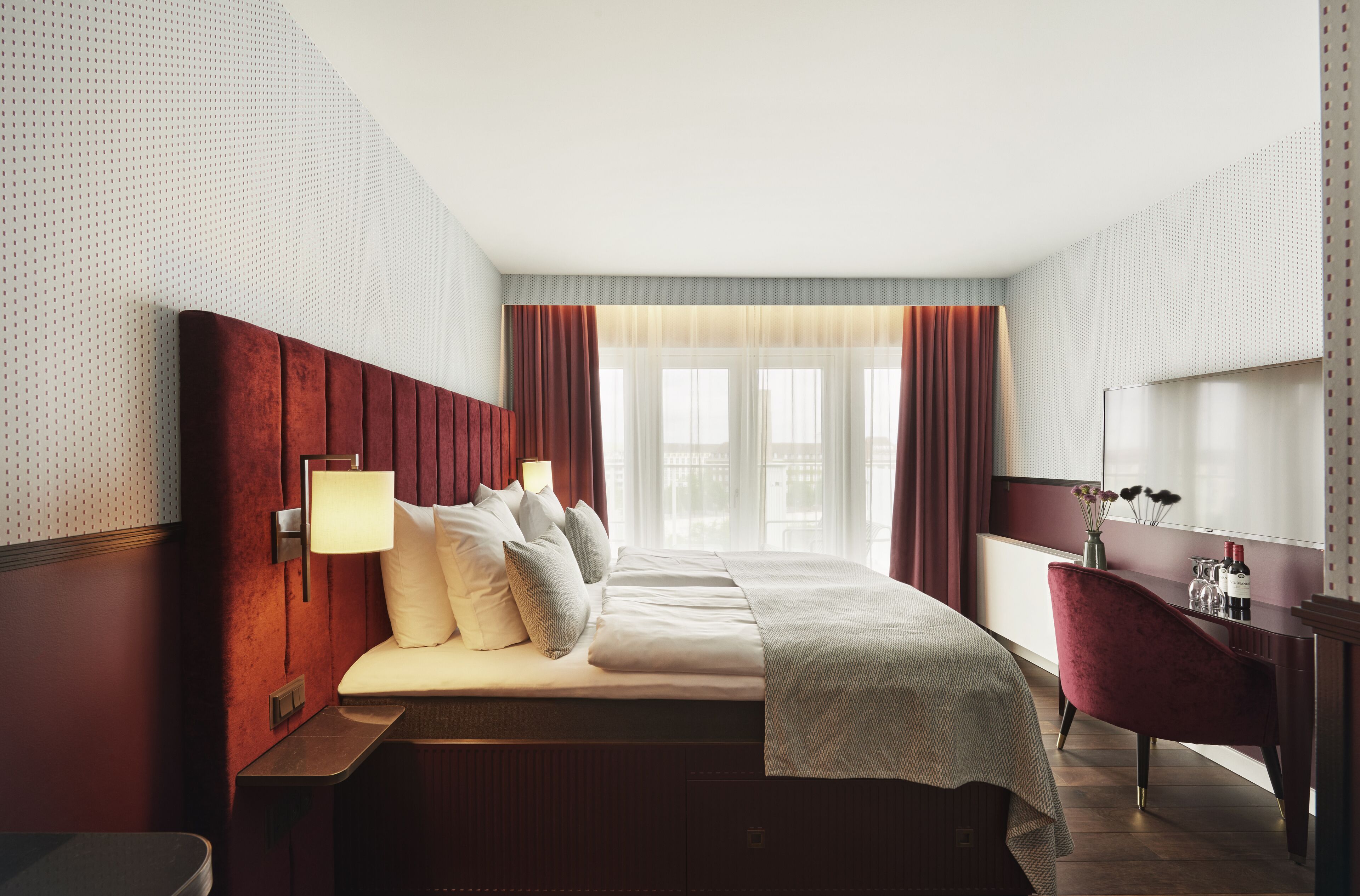 A hotel room with a large bed, a desk, and a view of the city through the window.