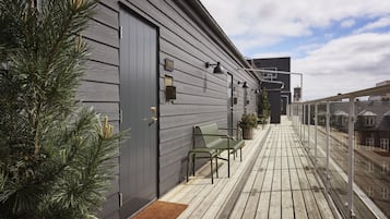 A wooden deck with two green chairs and a small table, a grey building with a door, and a clear sky.