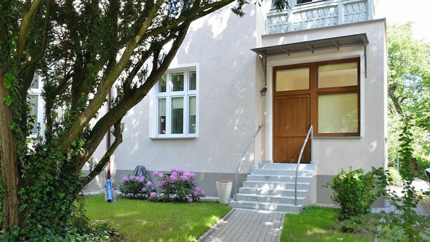 Una casa moderna de dos pisos con un camino empedrado que lleva a una puerta de madera y un conjunto de escaleras.