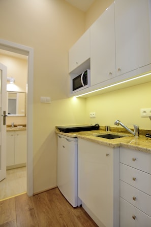 Una cocina compacta con microondas, lavamanos y armarios blancos.