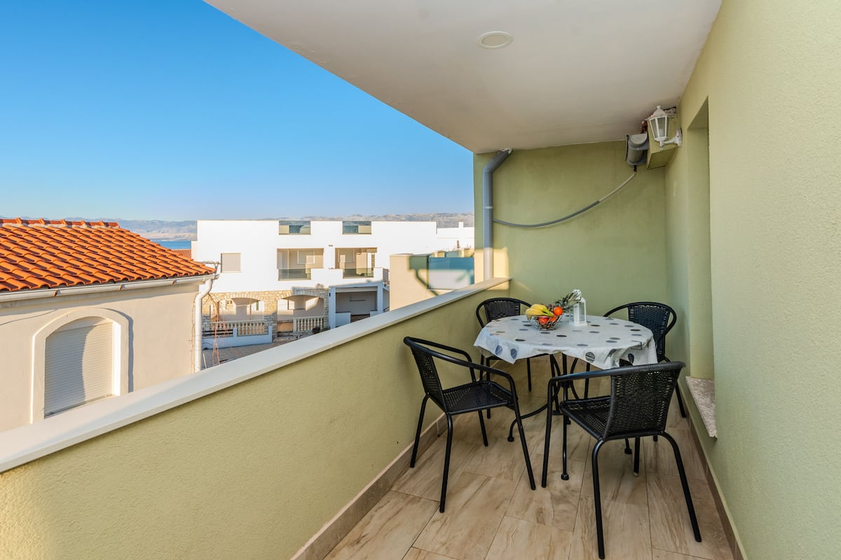 Ein Balkon mit Tisch und Stühlen, Blick auf Gebäude und ein klarer Himmel.