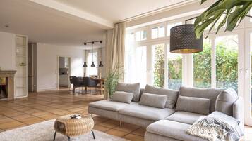 A spacious living room with a large grey sofa, a small ottoman, and a dining area in the background.