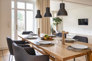 Uma sala de jantar com uma mesa de madeira posta para seis, cadeiras pretas e luminárias pendentes.