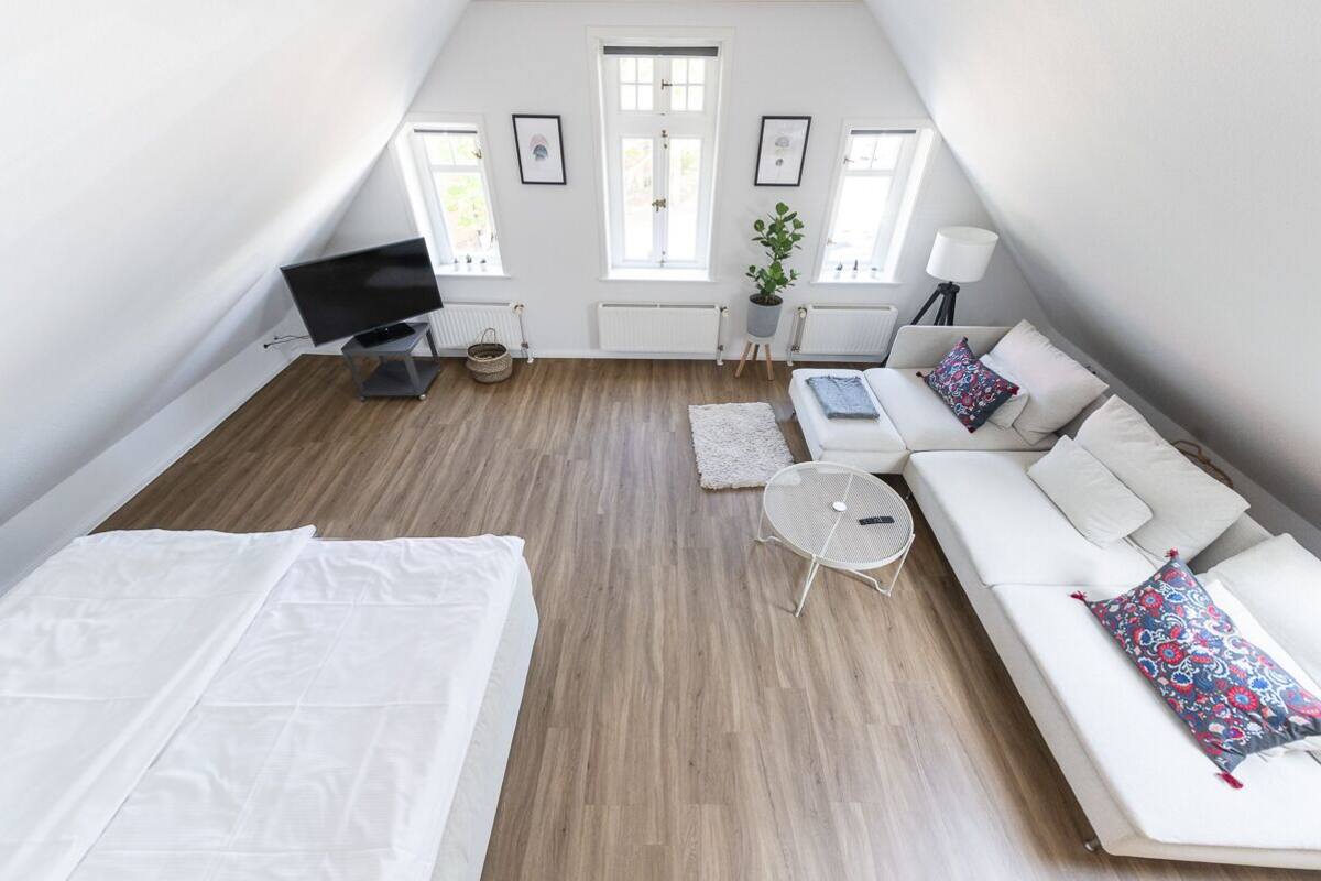 Un dormitorio estilo loft moderno con techo inclinado, cama, sofá, una mesita y televisor.