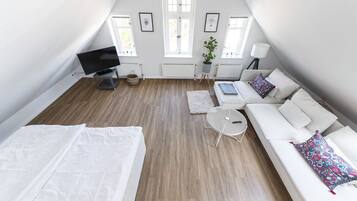 Un dormitorio estilo loft moderno con techo inclinado, cama, sofá, una mesita y televisor.