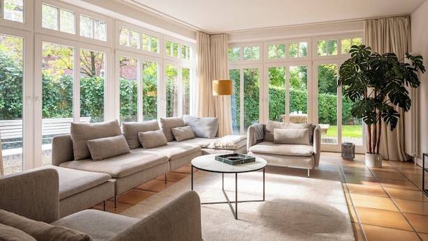 A spacious living room with a large sectional sofa, a round coffee table, and a view of a garden through large windows. - Altstadt Apartments Verden - Andreasstraße (Verden)