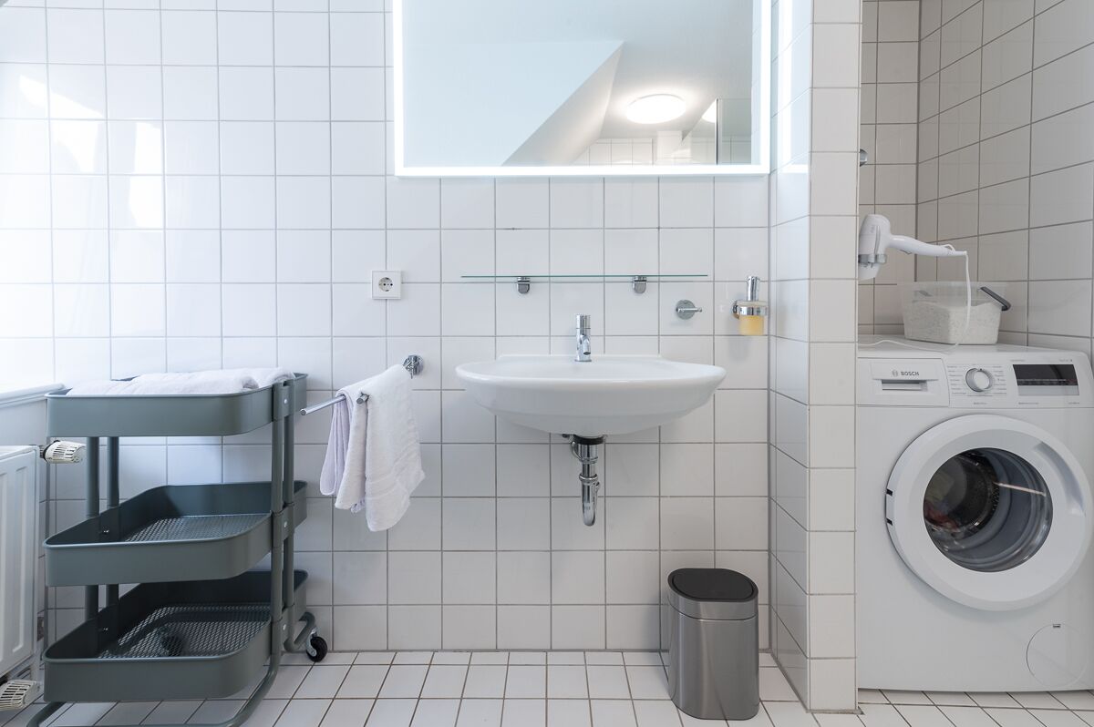 Un baño moderno con lavamanos, espejo, lavadora y tendedero.