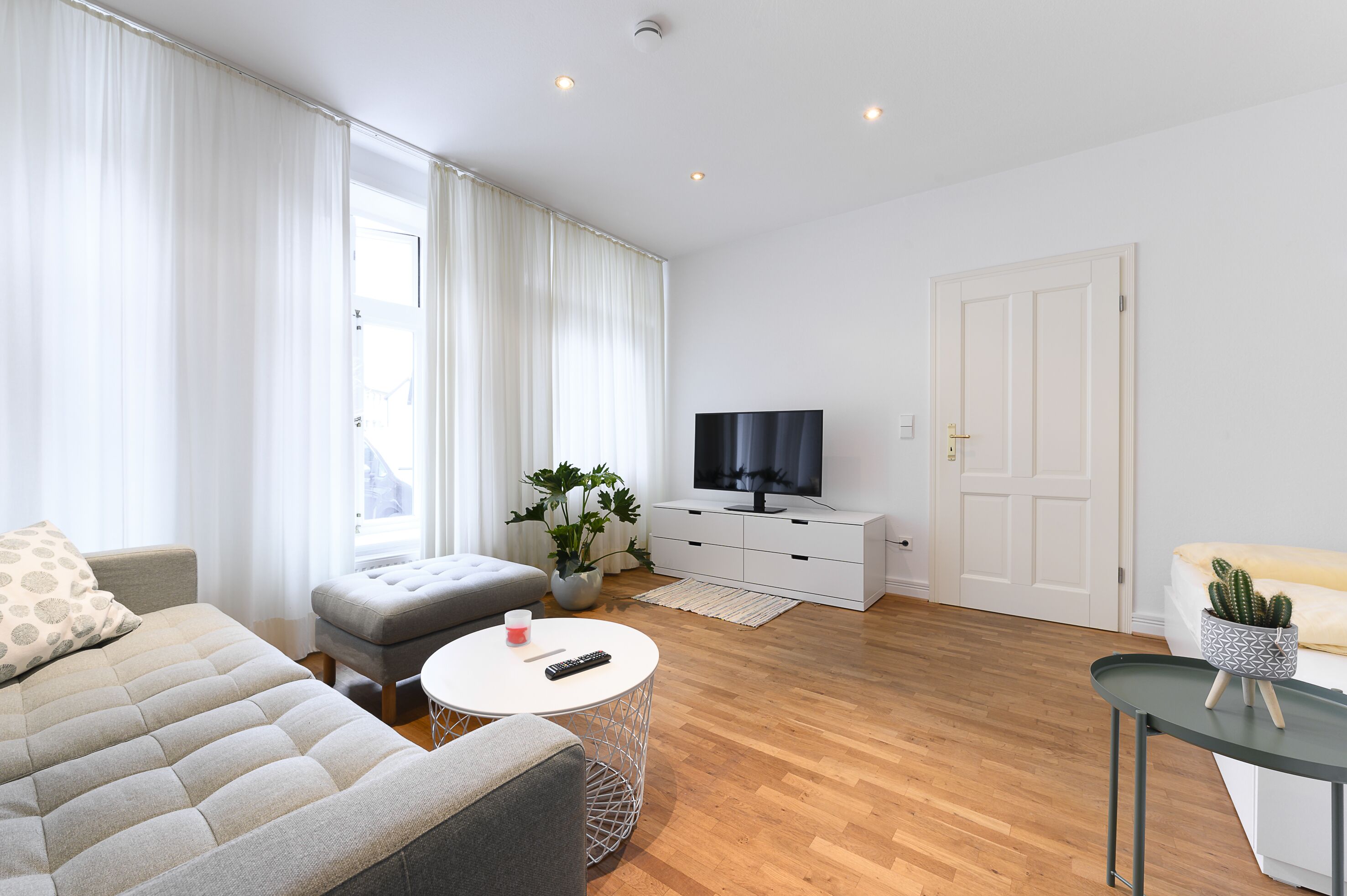 Ein modernes Wohnzimmer mit einer Couch, einem Hocker, einem runden Couchtisch und einem Fernseher auf einem weißen Schrank.