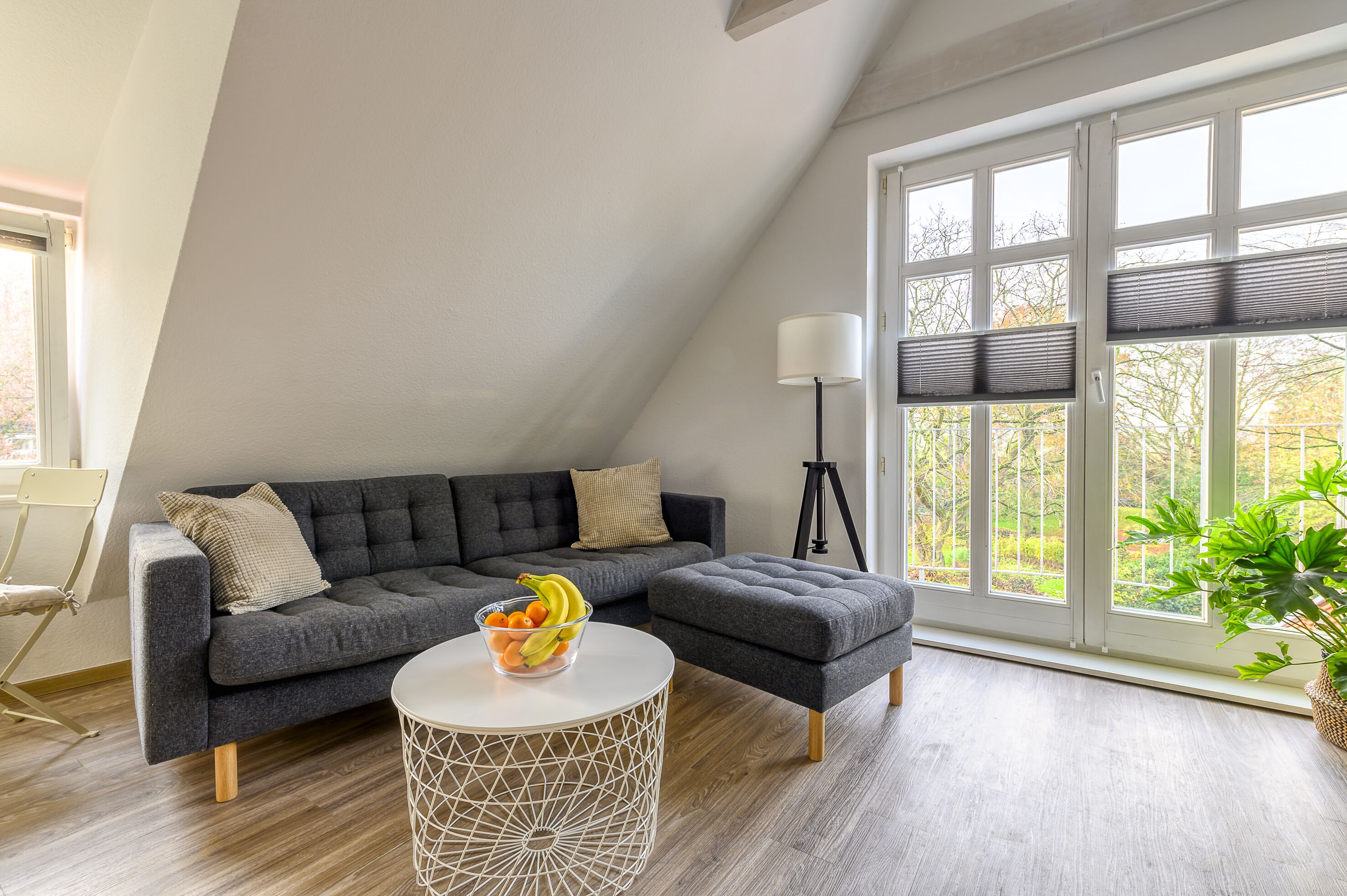 A modern living room with a grey sectional sofa, a round coffee table with a geometric design, and a large window with blinds.