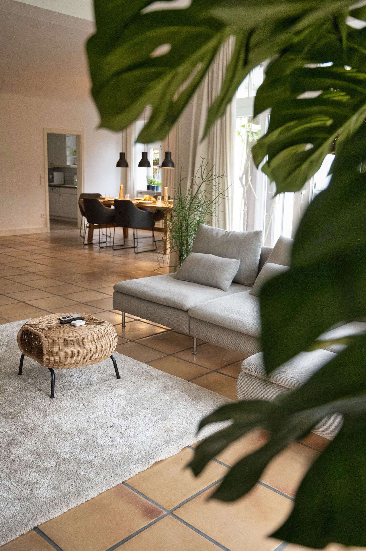 Un soggiorno moderno con un divano grigio, un pouf intrecciato e un'area da pranzo sullo sfondo.