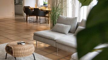 Un soggiorno moderno con un divano grigio, un pouf intrecciato e un'area da pranzo sullo sfondo.
