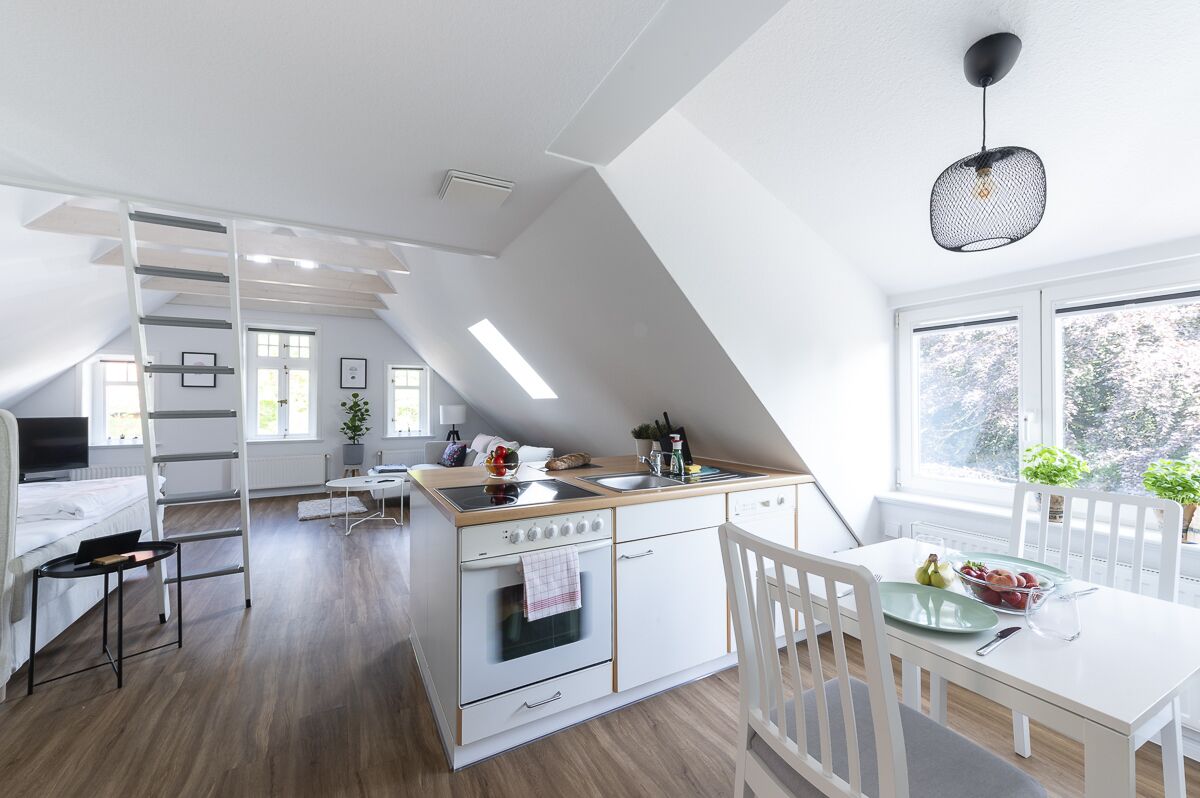 Una cocina moderna con una isla central, armarios blancos y una zona de comedor con mesa y sillas blancas.