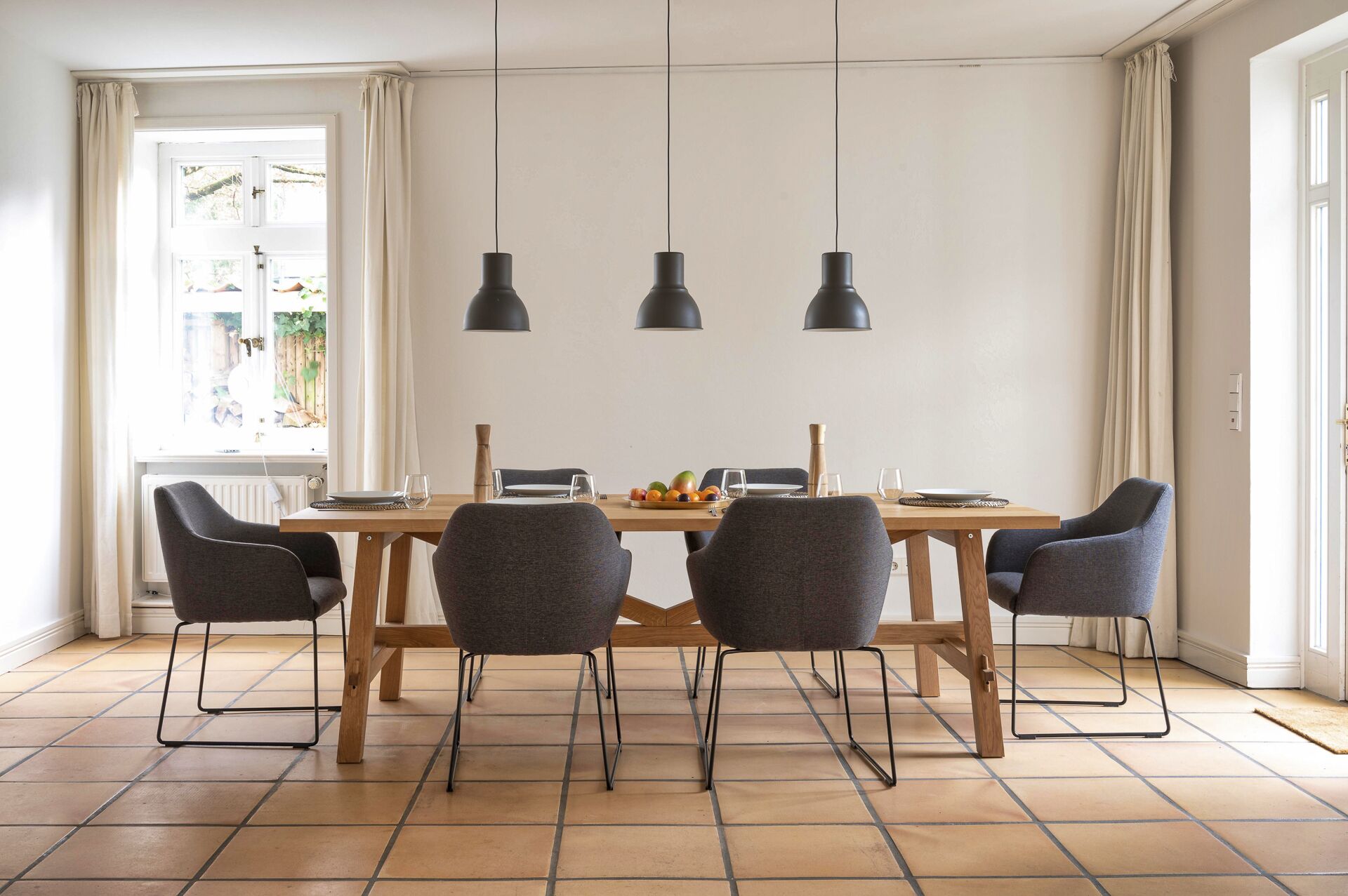 A dining area with a wooden table, four grey chairs, and three black pendant lights.