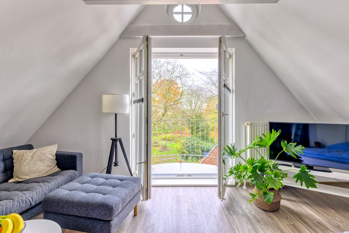 Un moderno loft con un gran ventanal, un sofá, un televisor y una planta en maceta.